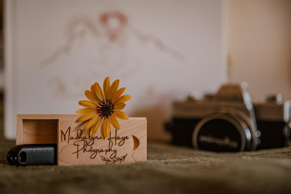 Personalized wooden USB box with engraved lettering displayed beside a camera and sunflower.