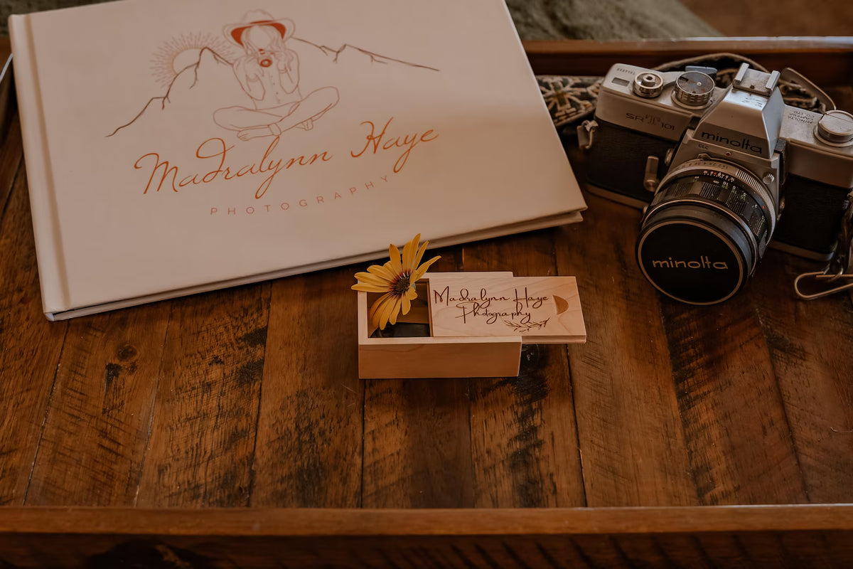 Custom engraved wooden USB memory box displayed on a rustic wooden table beside a camera and photo album.