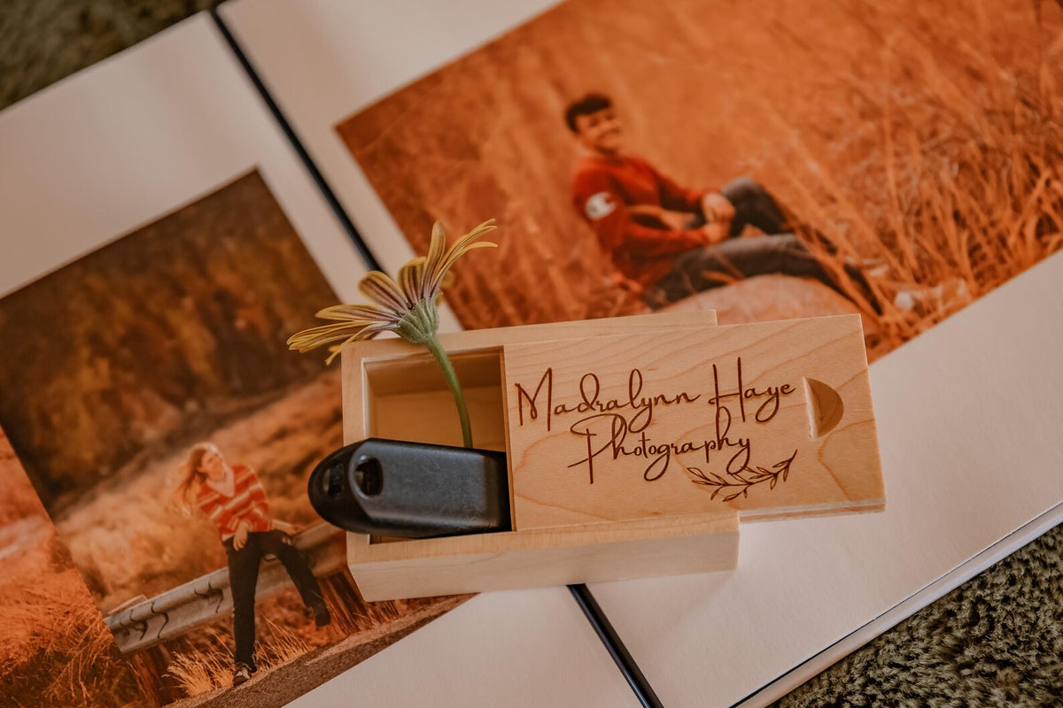 Custom engraved wooden USB storage box displayed beside printed photographs and a camera.