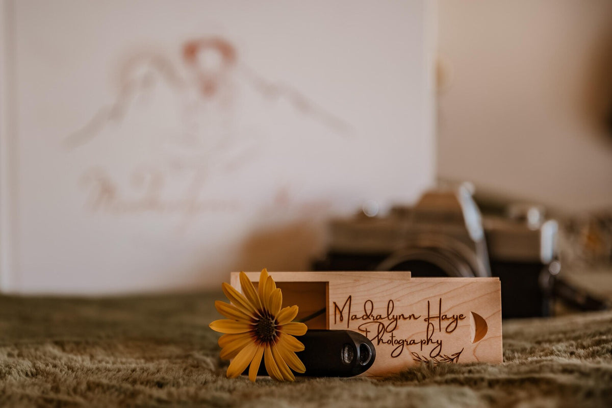 Close-up of a personalized wooden USB storage box with custom engraving and a USB drive beside a sunflower.