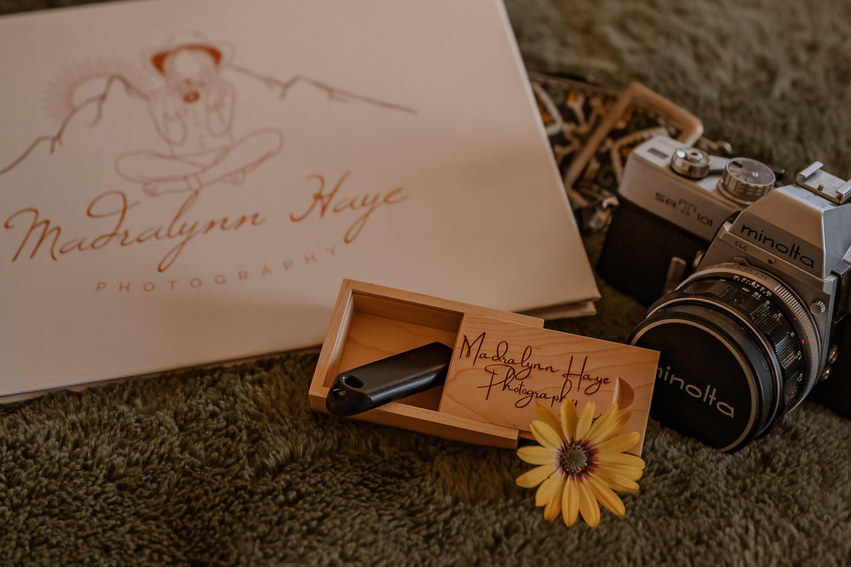Engraved wooden USB box arranged with a photography album and camera to preserve special memories.